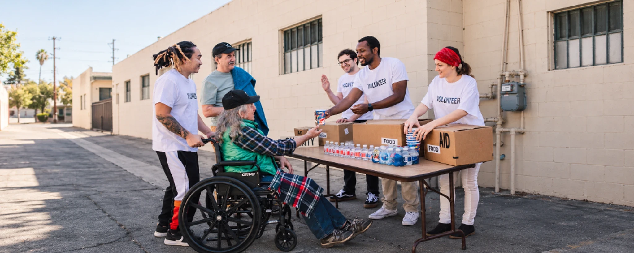 Volunteers at an outdoor table with boxes of food and bottled water.