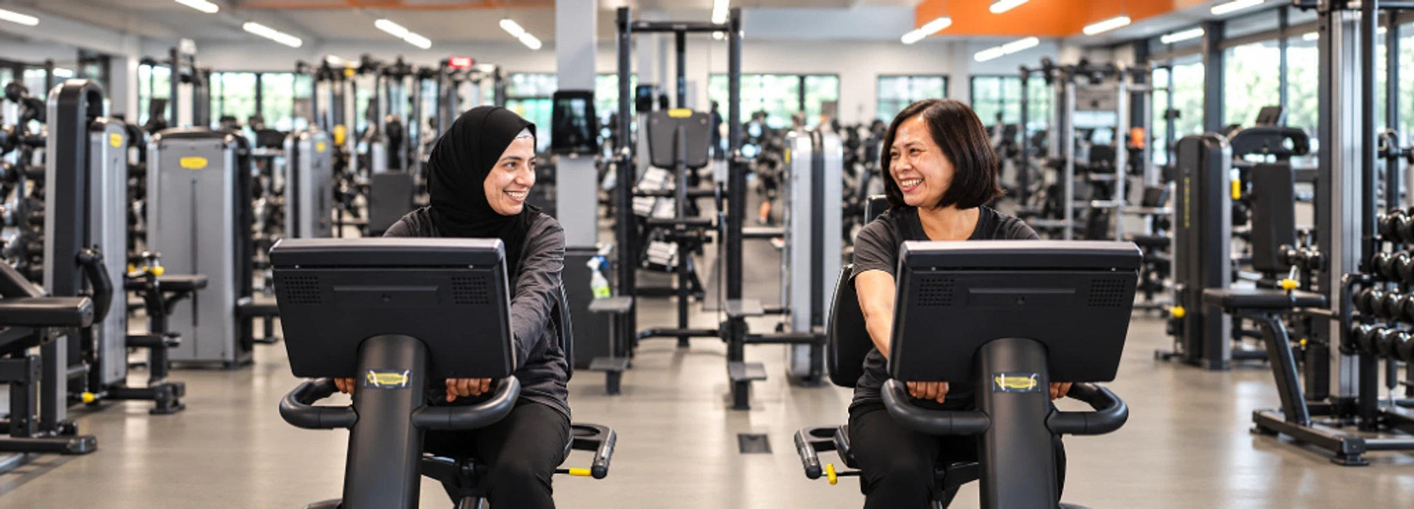 Two people on seated exercise machines in a gym.