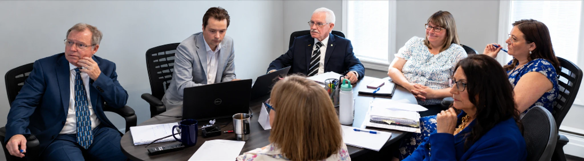 A group seated around an office meeting table with laptops and paperwork.